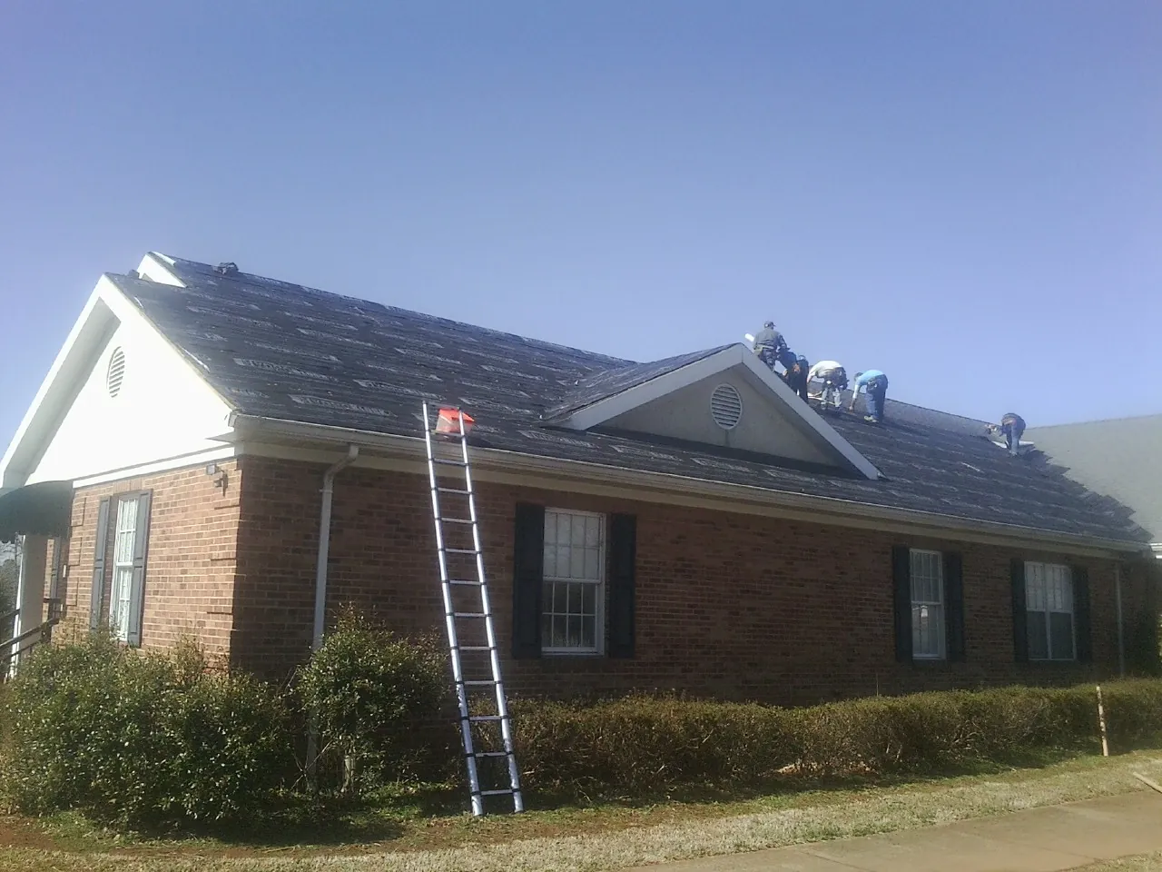 Crew tearing shingles off a brick ranch roof with a ladder set — Metal Roof Repair work by our crew in Machipongo
