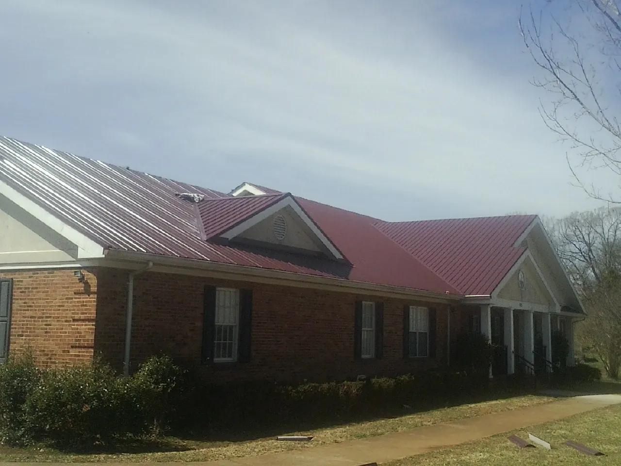 Red metal roof with gabled entries on a long brick building, from a Hail Damage Roof Repair job in Machipongo