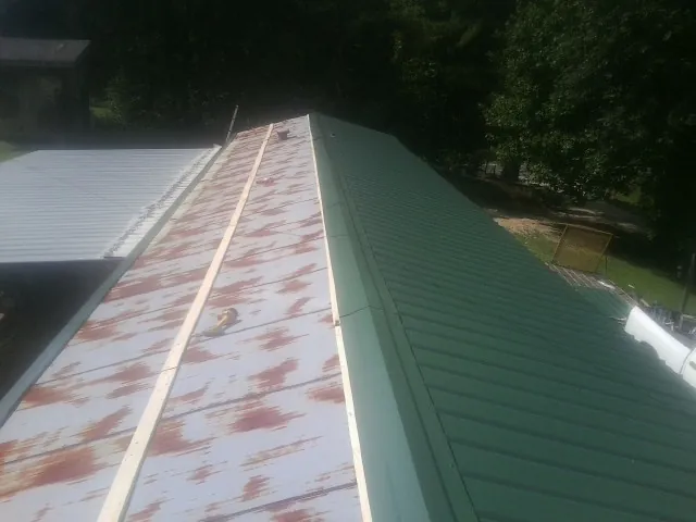 Old rusted panels beside newly installed green metal roofing — Wind Damage Roof Repair by Roofing Brothers in Machipongo