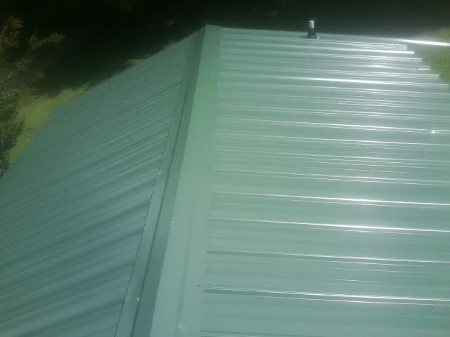 New green metal panels meeting at the ridge of a roof — Flat Roof Repair work by our crew in Machipongo